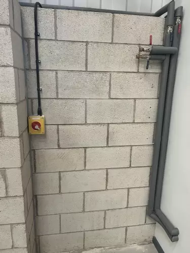 Bare block wall with existing pipes and electrical isolator before the wall-mounted pressure washer installation in Nottingham.